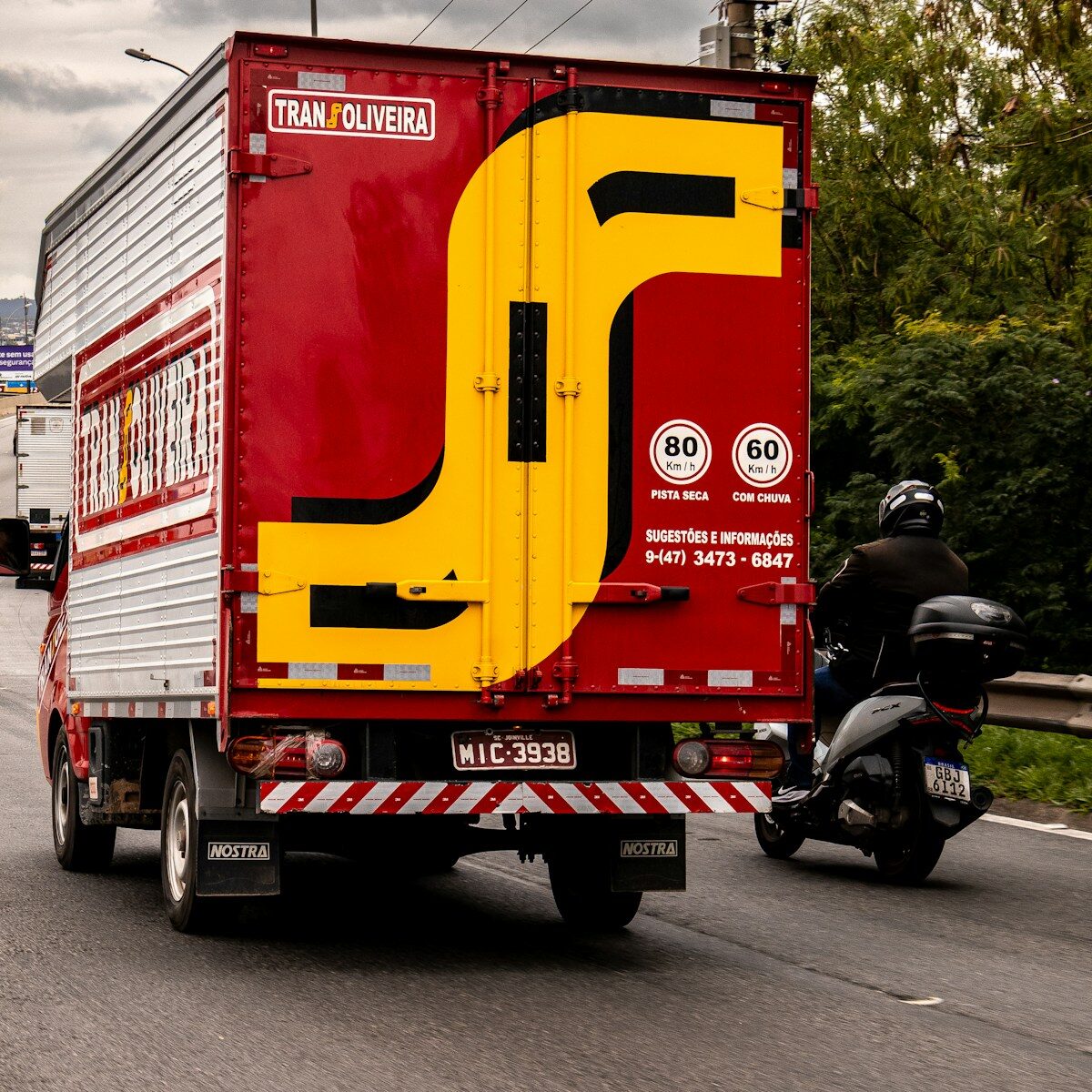 Red truck with yellow logo drives on road